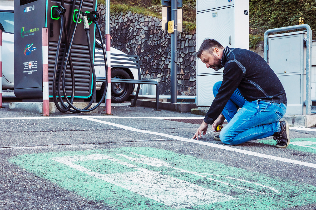 Independent L staff measuring an EV charging parking bay to assess accessibility for people with disabilities in South Tyrol.